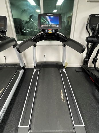 Indoor image of a treadmill with a digital display in a gym area.