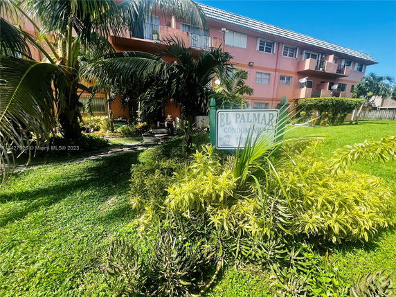 Front view of a multi-story condominium building with balconies and surrounding greenery.