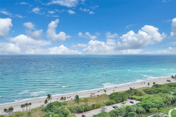 Panoramic view of a beach with blue ocean waves and scattered clouds in the sky.