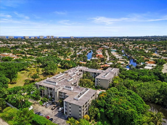 Aerial view of a large residential building surrounded by greenery with a cityscape in the background.
