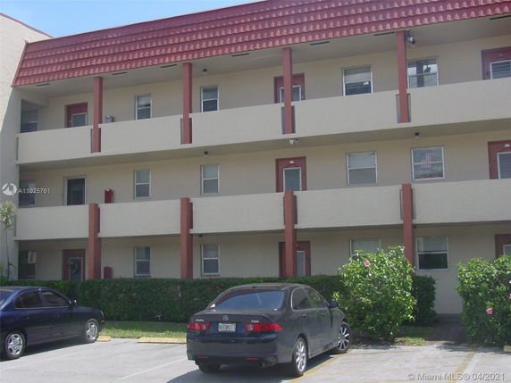 Front view of a three-story residential building with balconies and parked cars in front.