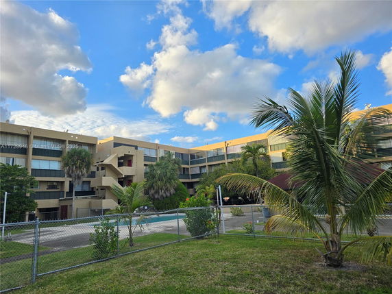 Front view of a multi-story residential building with balconies and surrounding palm trees.