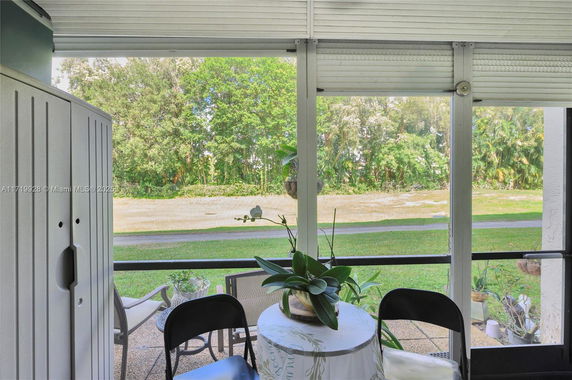 View of a grassy area and trees from a screened-in porch with a small table and two chairs.