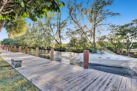 View of a dock beside a canal with a boat moored and trees in the background.