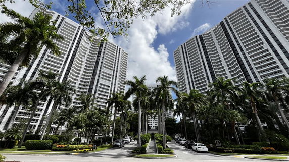 View of tall residential buildings with multiple balconies and palm trees in front.