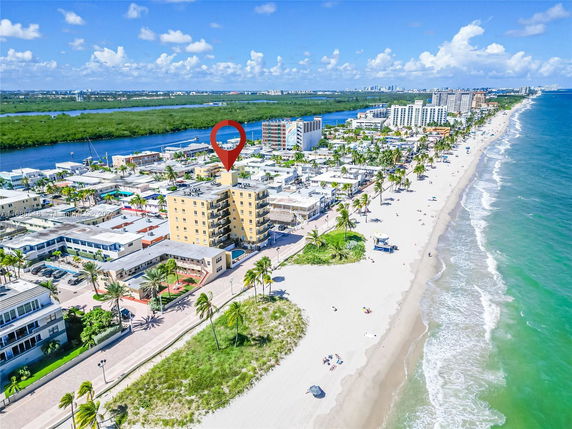 Aerial view of a coastline with multiple multi-story buildings, a sandy beach, and a body of water.