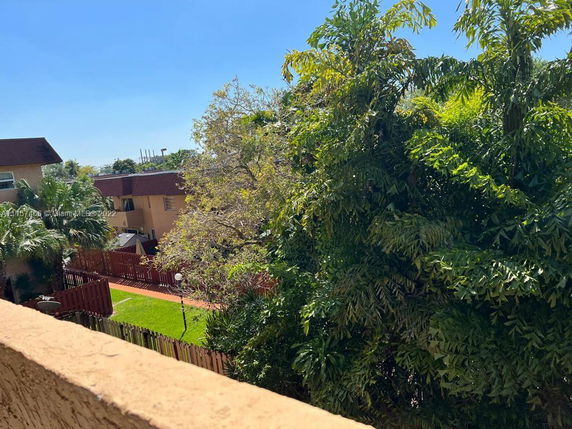 View of residential buildings with trees and a fenced yard.