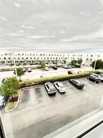 View of a parking area with multiple cars parked in designated spaces in front of a row of buildings.