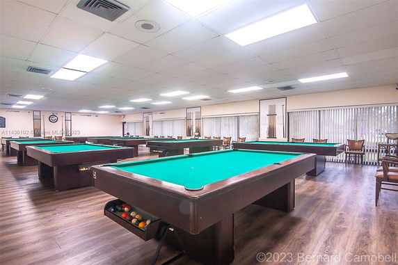 Room with multiple pool tables and chairs arranged around.