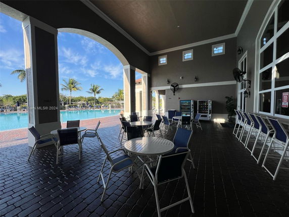 View of a clubhouse patio area with tables and chairs, overlooking a swimming pool.