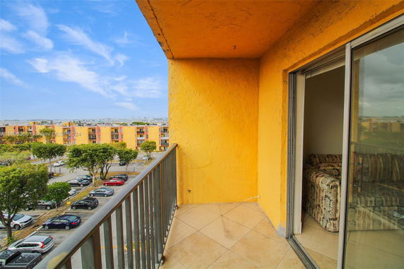 View from a balcony with yellow walls, overlooking parking area and buildings.