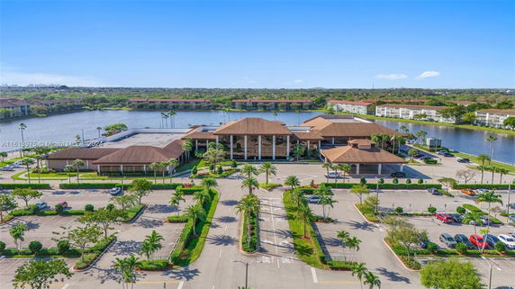Building complex with brown roofs surrounded by parking areas and a body of water in the background.