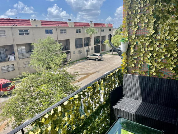 View from a balcony overlooking a parking area and adjacent buildings.