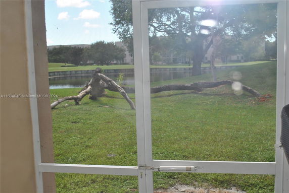 View through a window showing a grassy area with a fallen tree branch and a pond in the background.