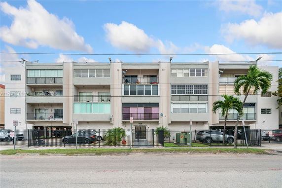 Front view of a multi-story apartment building with balconies and parking area.