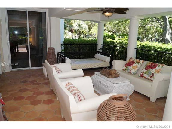Covered outdoor seating area with couches and a coffee table, overlooking greenery.