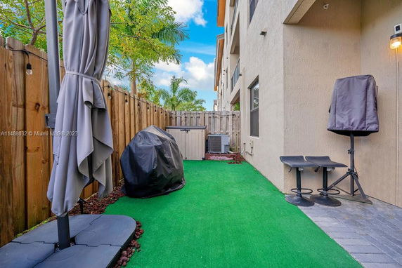 Outdoor area adjacent to a building with artificial grass, fenced with wooden panels.