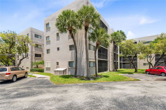 Front view of a multi-story residential building with parking area and palm trees.