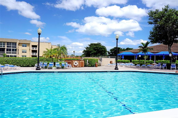 Outdoor swimming pool with surrounding lounge chairs and a building in the background.