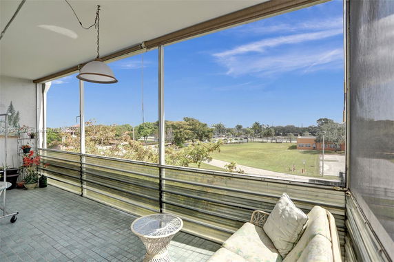 Panoramic view from a covered balcony overlooking a park and buildings.