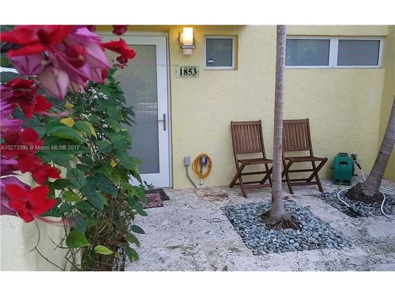 Front view of a house entrance with a stone floor, chairs, and small palm trees.