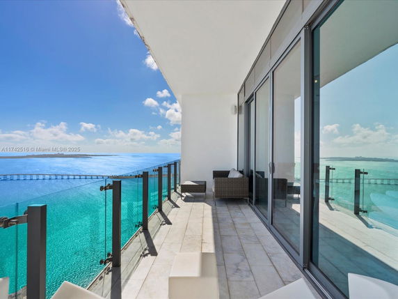View from a balcony overlooking the ocean with glass railing and seating area.