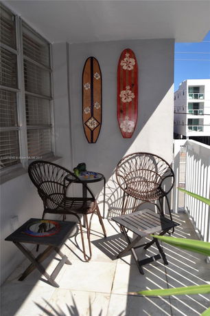 Small outdoor balcony with two chairs, a small table, and wall decorations resembling surfboards.