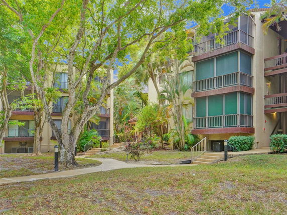 Front view of multi-story residential buildings with balconies and surrounded by trees.