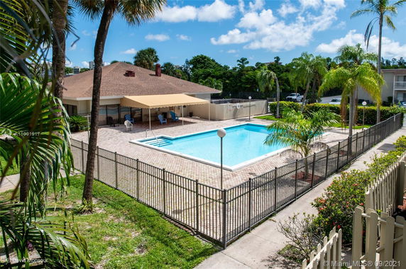 Outdoor view of a swimming pool area with fenced patio and adjacent building with a canopy.