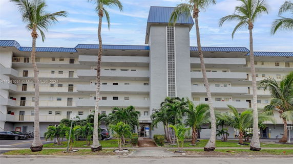 Front view of a multi-story residential building with balconies and palm trees.