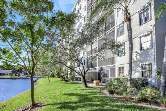 Side view of a multi-story building next to a pond with trees and grass.