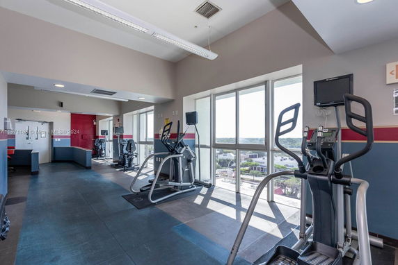 Indoor gym area with various exercise machines and large windows.