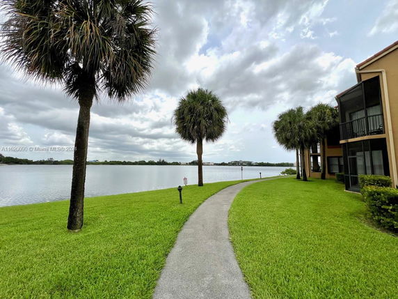 Pathway beside a lake with palm trees and part of a building visible.