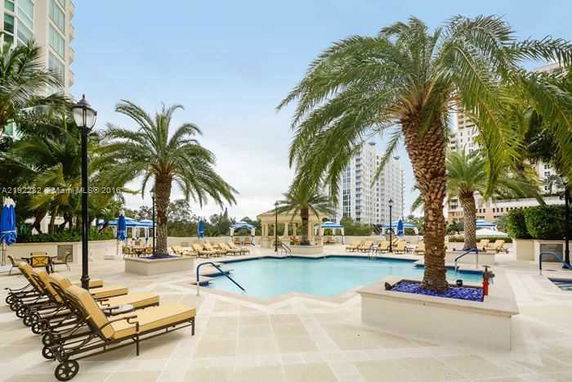 Outdoor swimming pool area with lounge chairs and palm trees.