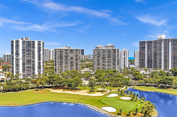 Panoramic view of several high-rise buildings with a golf course and water feature in the foreground.