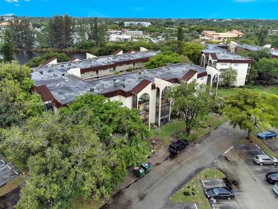 Aerial view of a multi-story apartment complex surrounded by trees and a parking area.