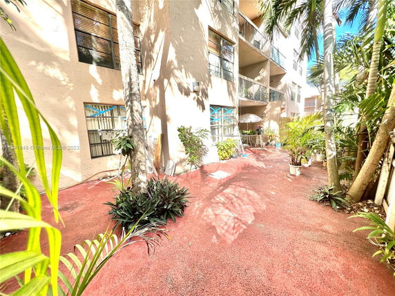 View of a multi-story building with balconies and a red patio area surrounded by tropical plants.