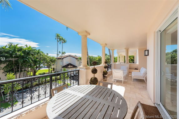 View from a balcony with a round table and chairs, overlooking nearby buildings and lush greenery.