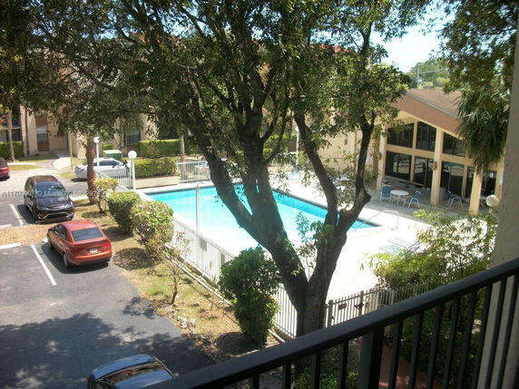 View of a swimming pool area surrounded by buildings and parked cars.