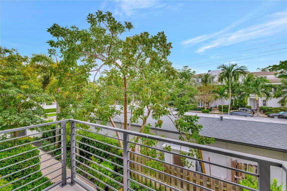 A view from a balcony overlooking a street with houses and trees.