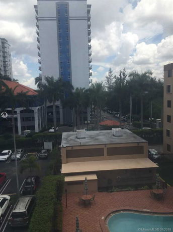 View of a high-rise building with a swimming pool and parking area in the foreground.