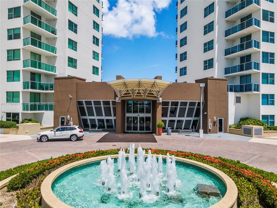 Front view of a high-rise building with a modern entrance and a circular fountain in front.