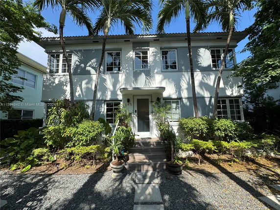 Front view of a two-story house with palm trees and shrubbery.