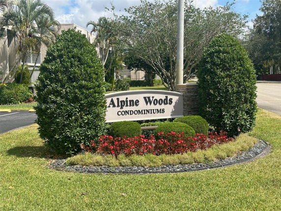 Front view of a condominium building with landscaping and a sign reading 'Alpine Woods Condominiums'.