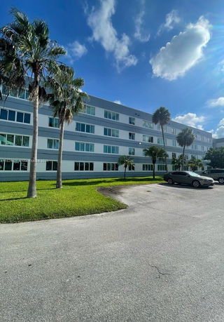 Front view of a multi-story building with large windows and palm trees in front.