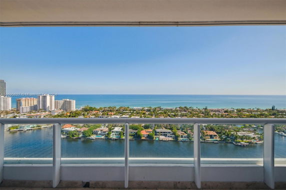 View from a high-rise balcony overlooking a waterfront area with residential buildings and the ocean in the distance.