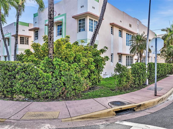 Front view of a building with multiple windows and palm trees around.