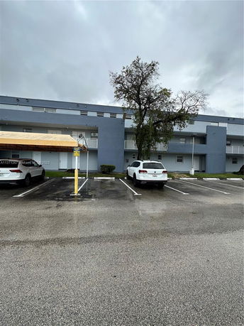 Outdoor parking area with cars in front of a multi-story building.