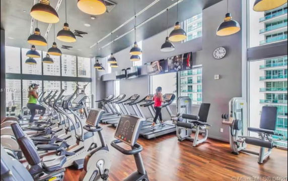 Interior view of a gym with various exercise equipment and large windows.
