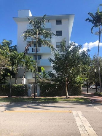 Front view of a multi-story building with balconies and surrounded by palm trees.
